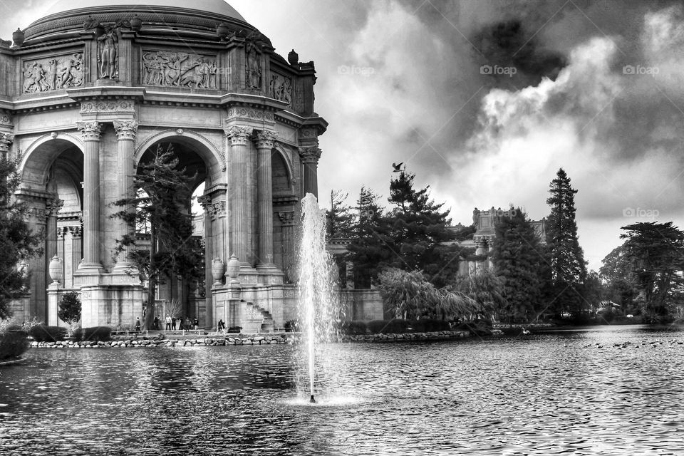 Black and white image of the palace of fine arts in San Francisco California on a cloudy day with the fountain going in the lagoon 