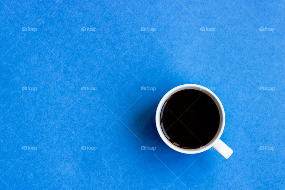 Top view to white cup of black coffee to the blue background. Copy space.