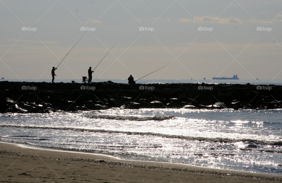silhouettes of three fishermen on the rocks in One sunny day by the sea near the  beach