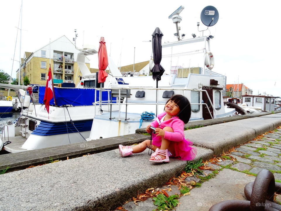 Little girl sitting near harbor with camera
