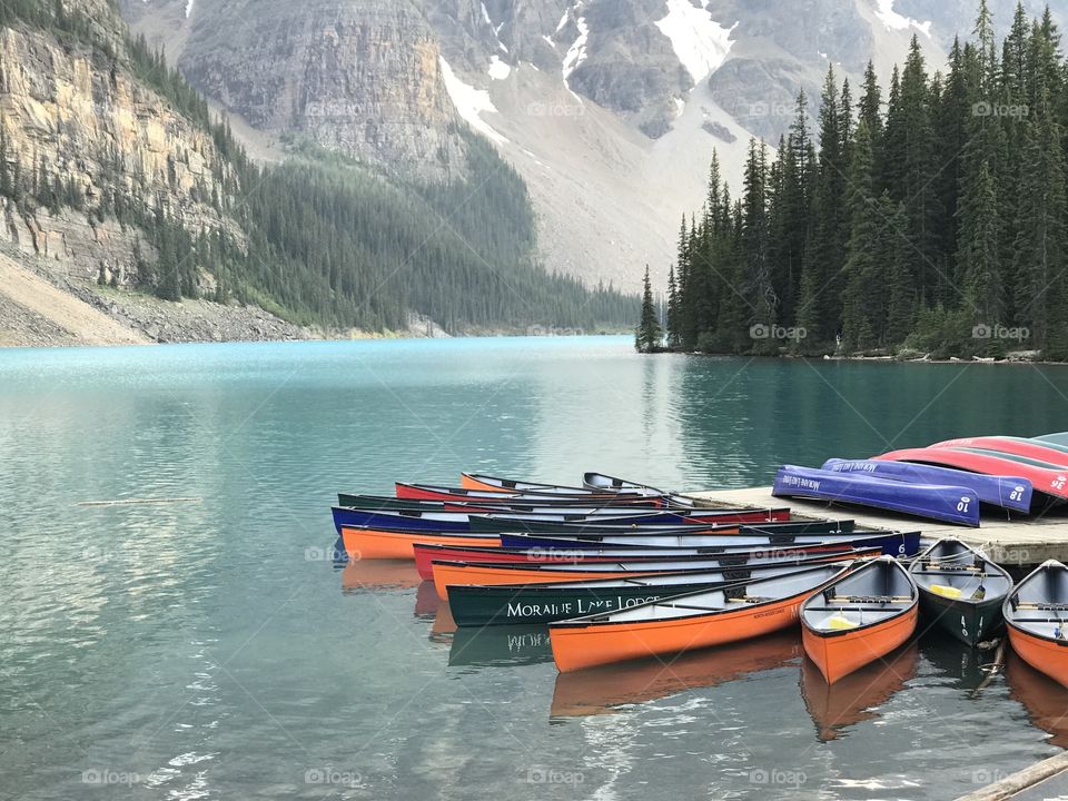 Colorful canoes on Moraine Lake, floating on turquoise water.  Mountains and trees surround the lake. 