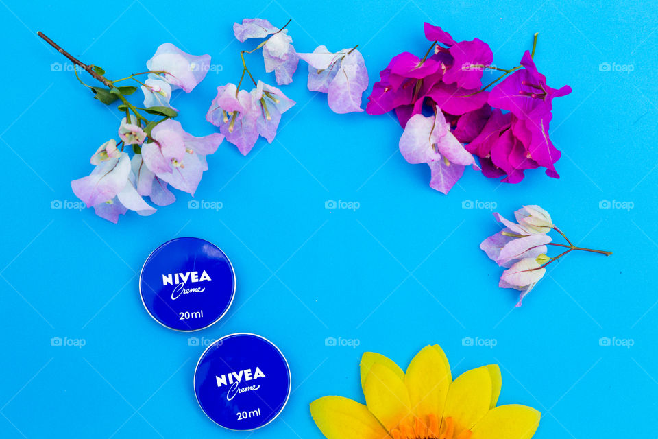 nivea creme tin and bougainvillea flowers on blue background flatlay