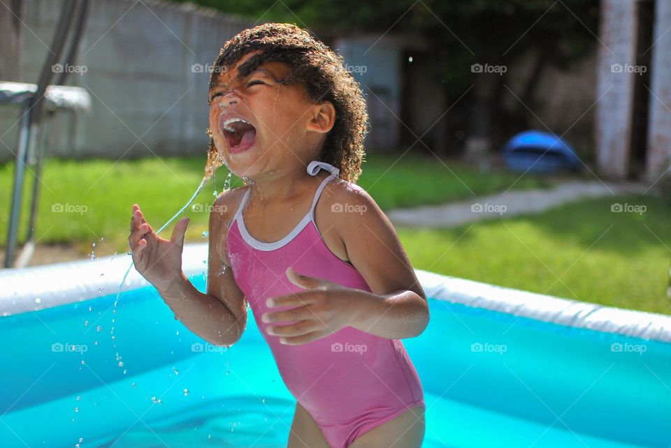 Cute little girl enjoying some playtime in a swimming pool during a hot summer day, looking for refreshment