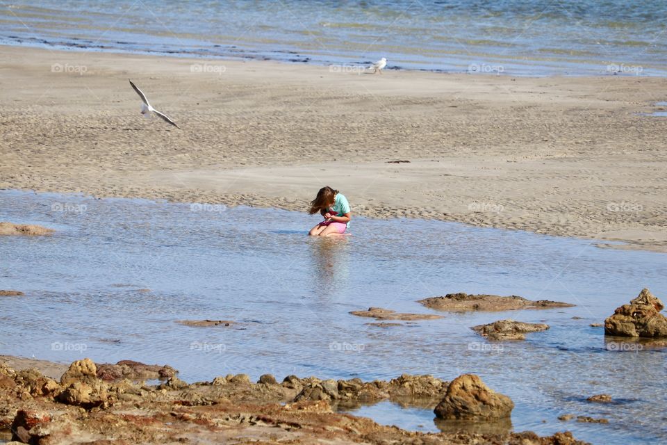 Little girl kneeling in tidal pool at ocean on beach