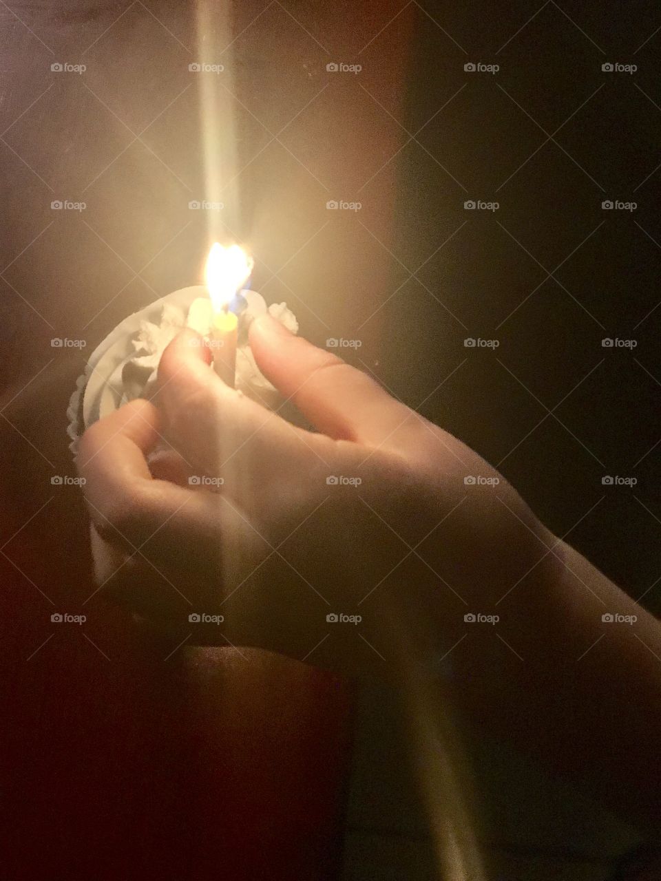 A hand holding a birthday candle on top of a chocolate cupcake covered with white vanilla frosting celebrating a birthday. USA, America