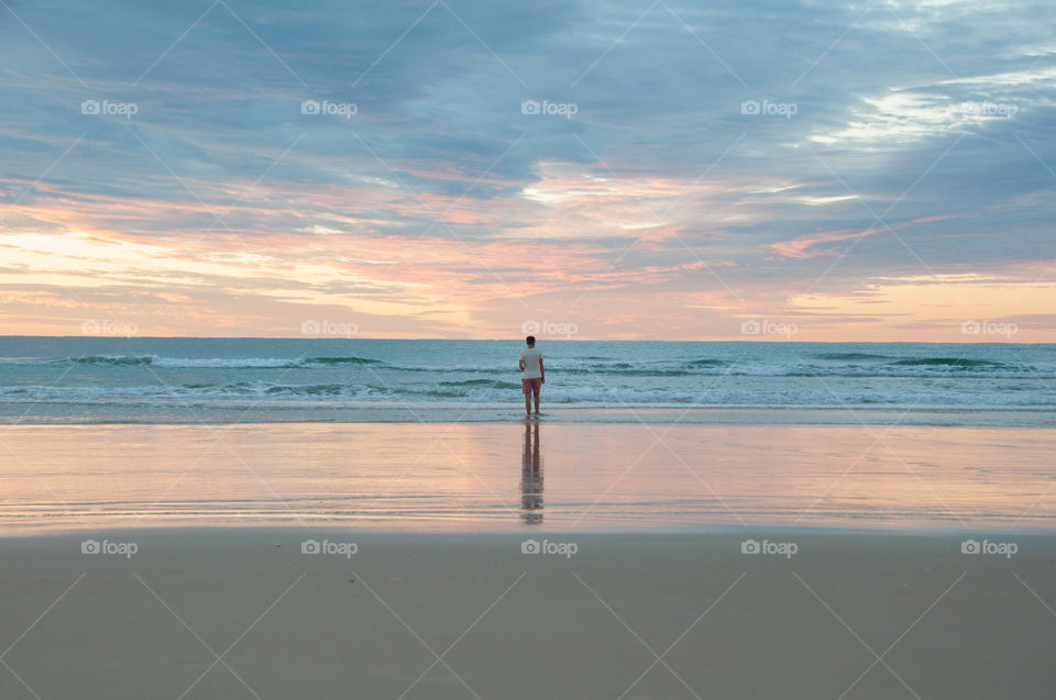 Rear view of a man standing on beach at sunrise