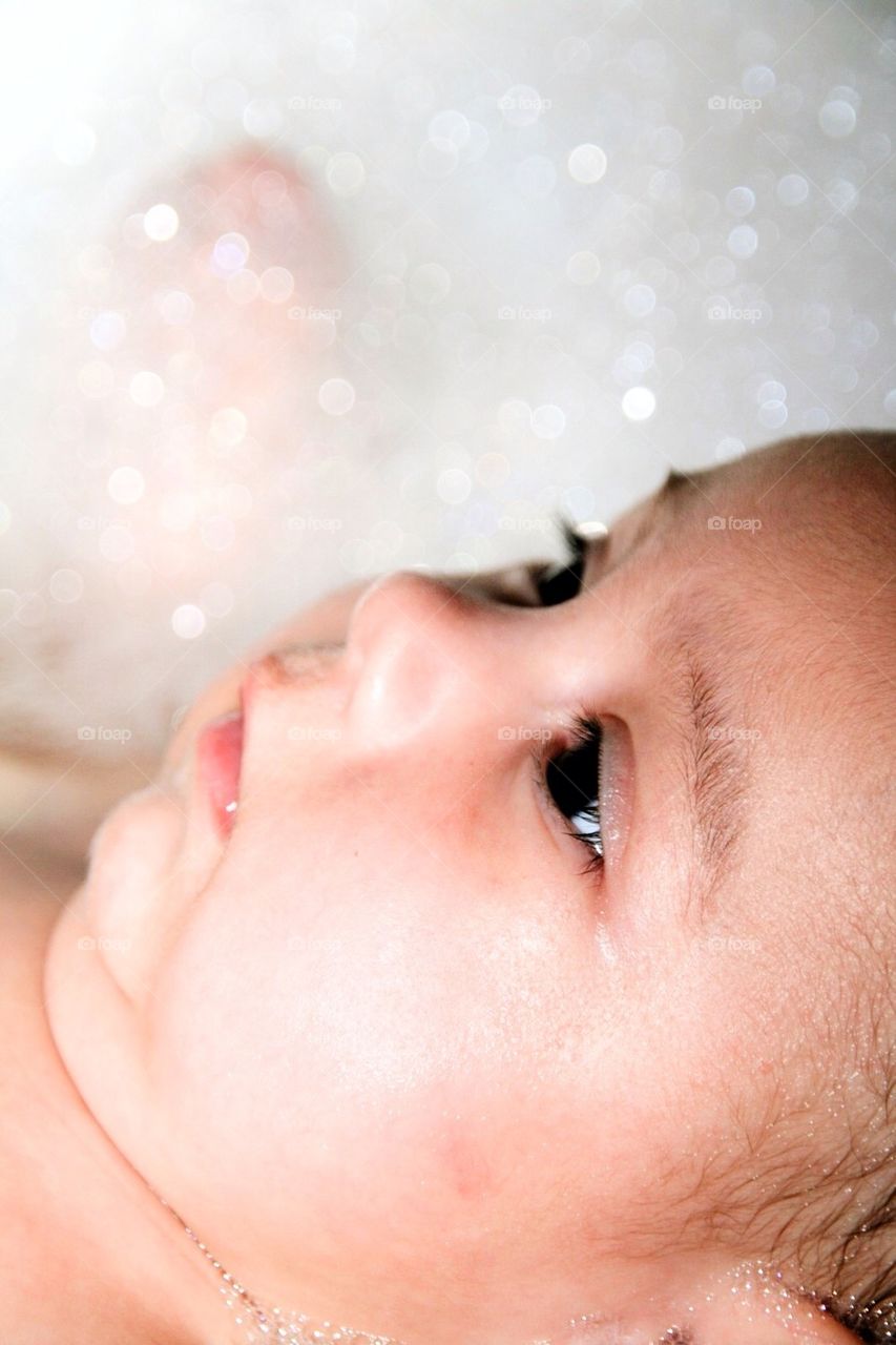 Baby girl is looking up in a bath of foam