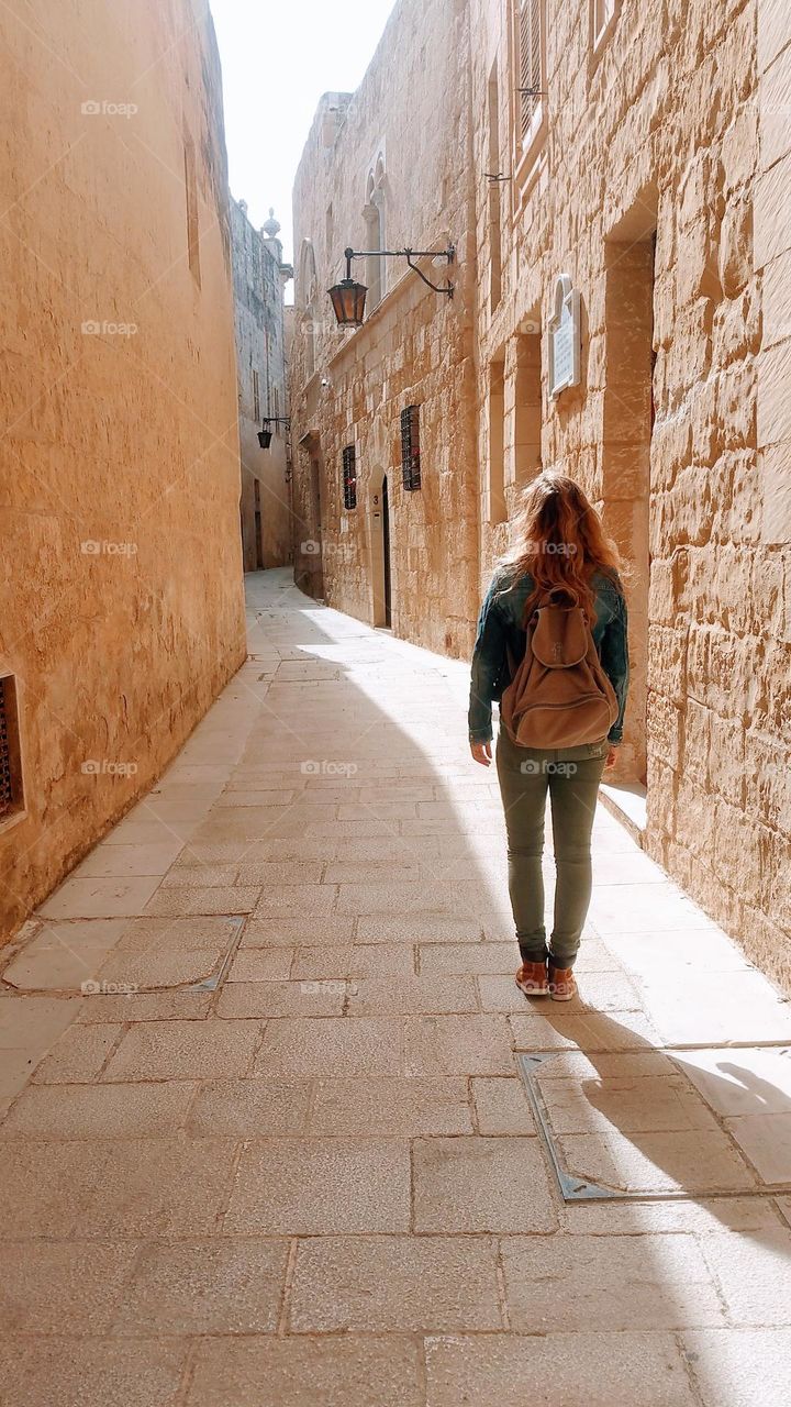 woman with long hair and backpack walking trough a small street in an old town at Malta