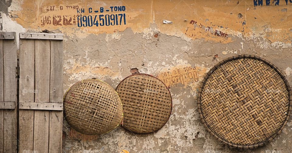 A worn outside wall with hanging wicker baskets and lids in Hanoi, Vietnam.