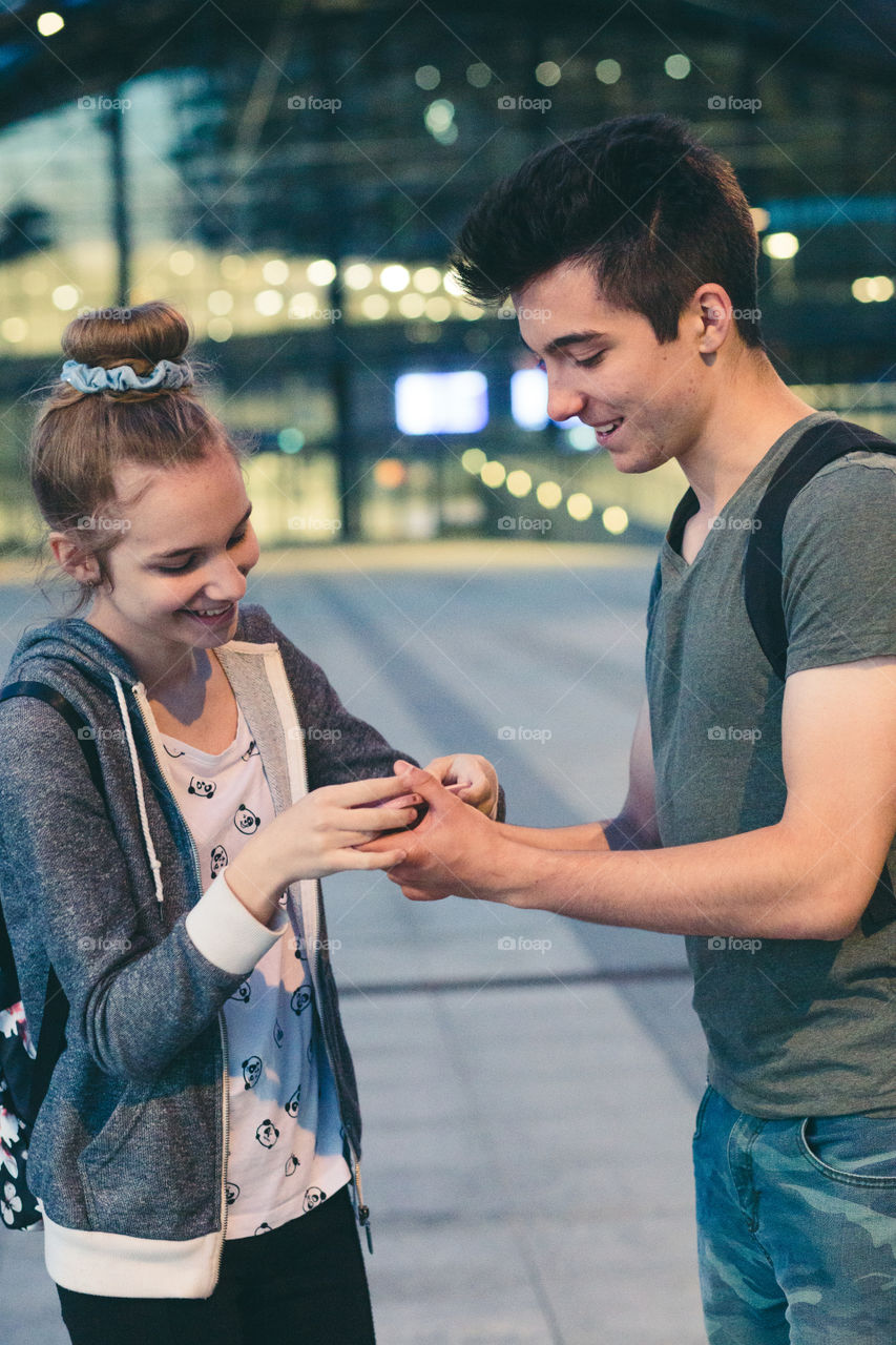 Young woman and man looking at screen of smartphone during walk in the city at night