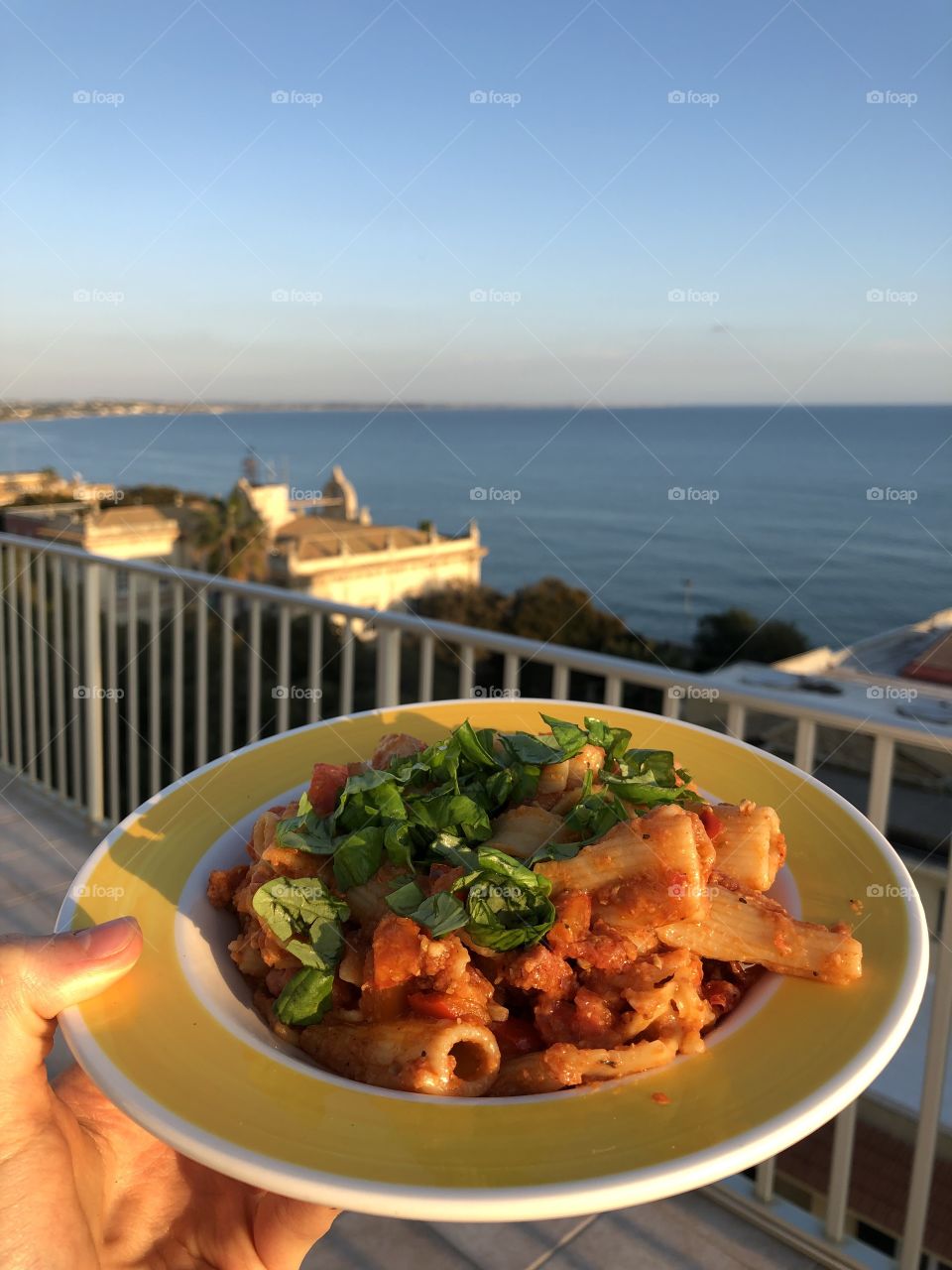 Enjoying a wonderful bowl of red pesto pasta salad with red peppers, tomatoes, chorizo (turkey), seasoned with oregano and Italian herbs in Pozzallo, Sicily (Italy) with a stunning view of the Mediterranean Sea.
