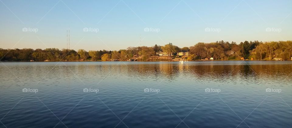 a cabin surrounded by trees on a lakeshore at sunset