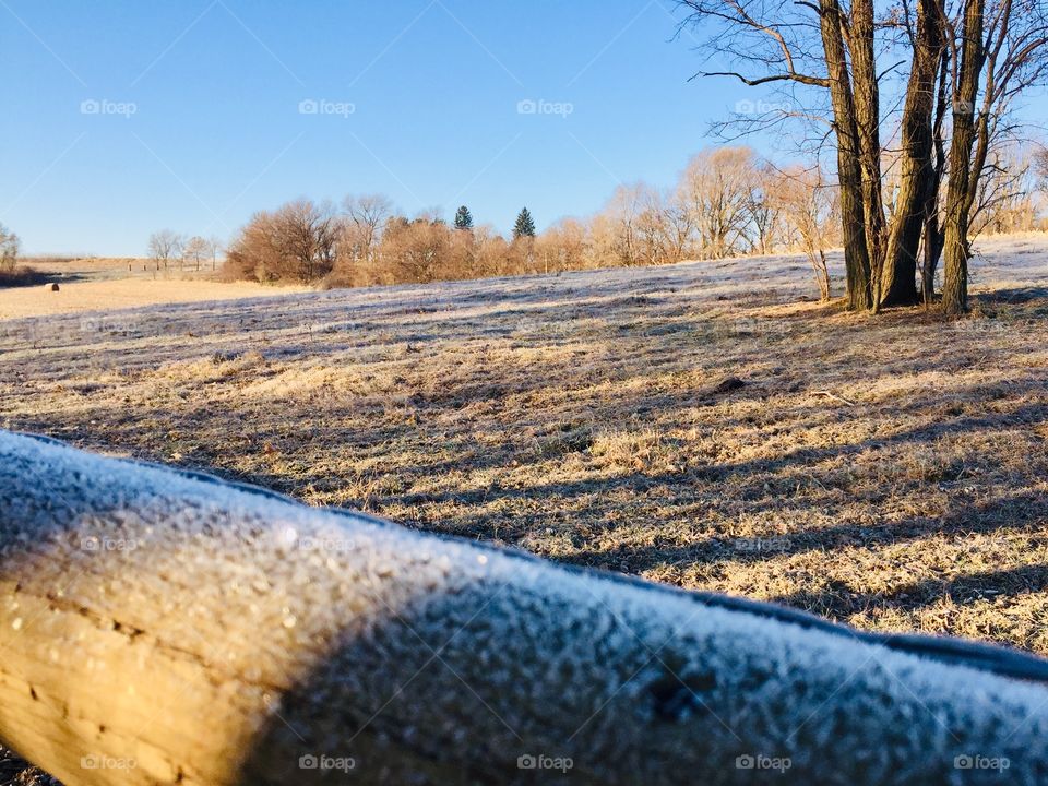 Frost crystals on a wooden fence rail, beautiful rural landscape visible in the distance across dried brown field grass in autumn 