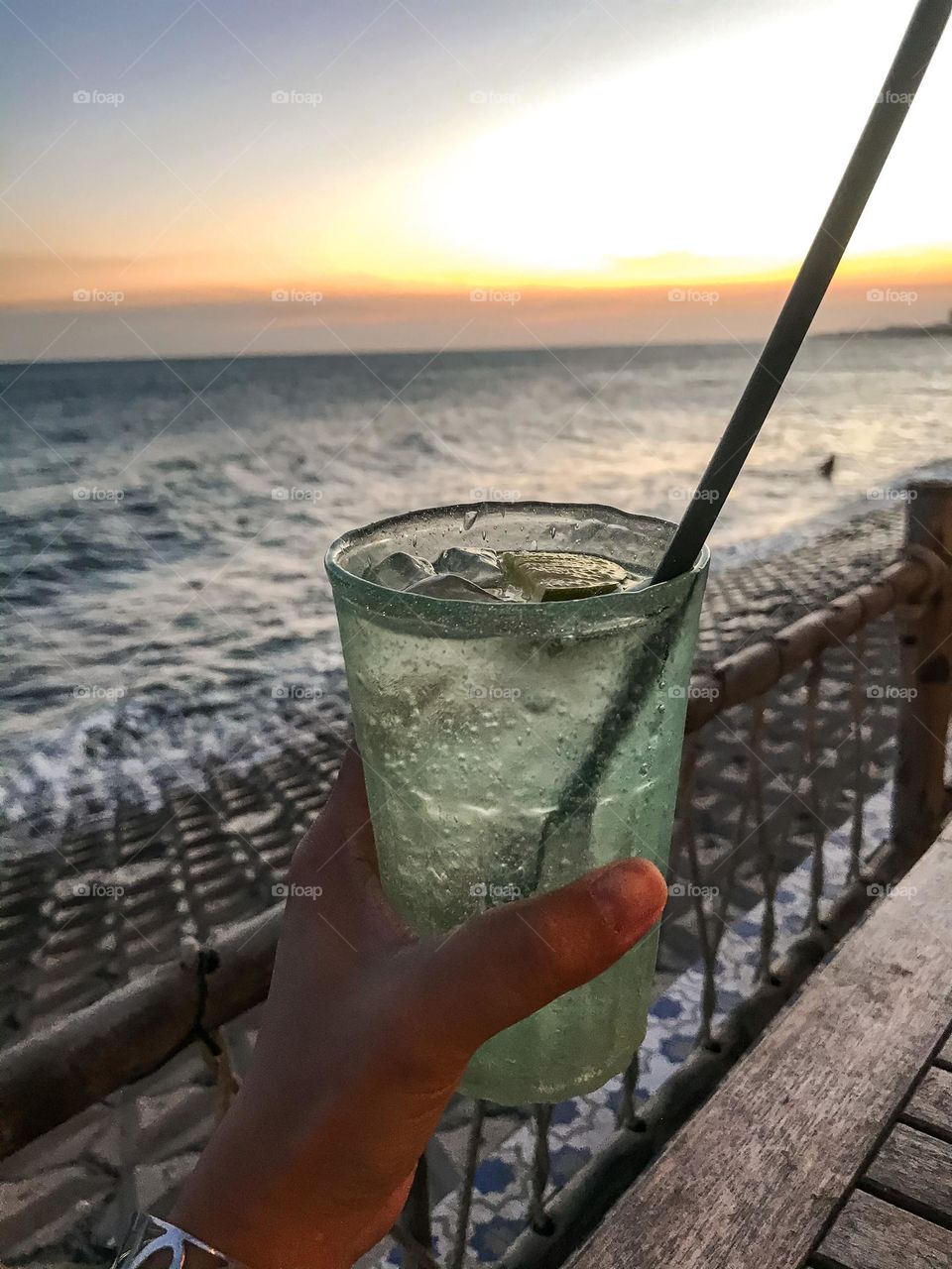 Hand holding a glass of cold water at a seaside restaurant at sunset , sunset landscape 