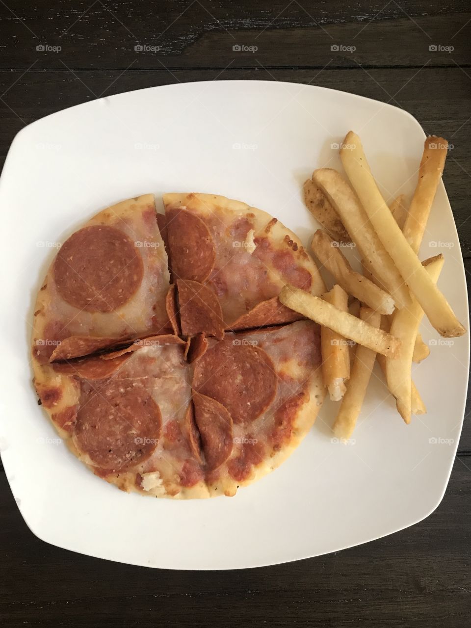 Delicious and cheesy pepperoni pizza and fries displayed on a white plate for dinner. USA, America 