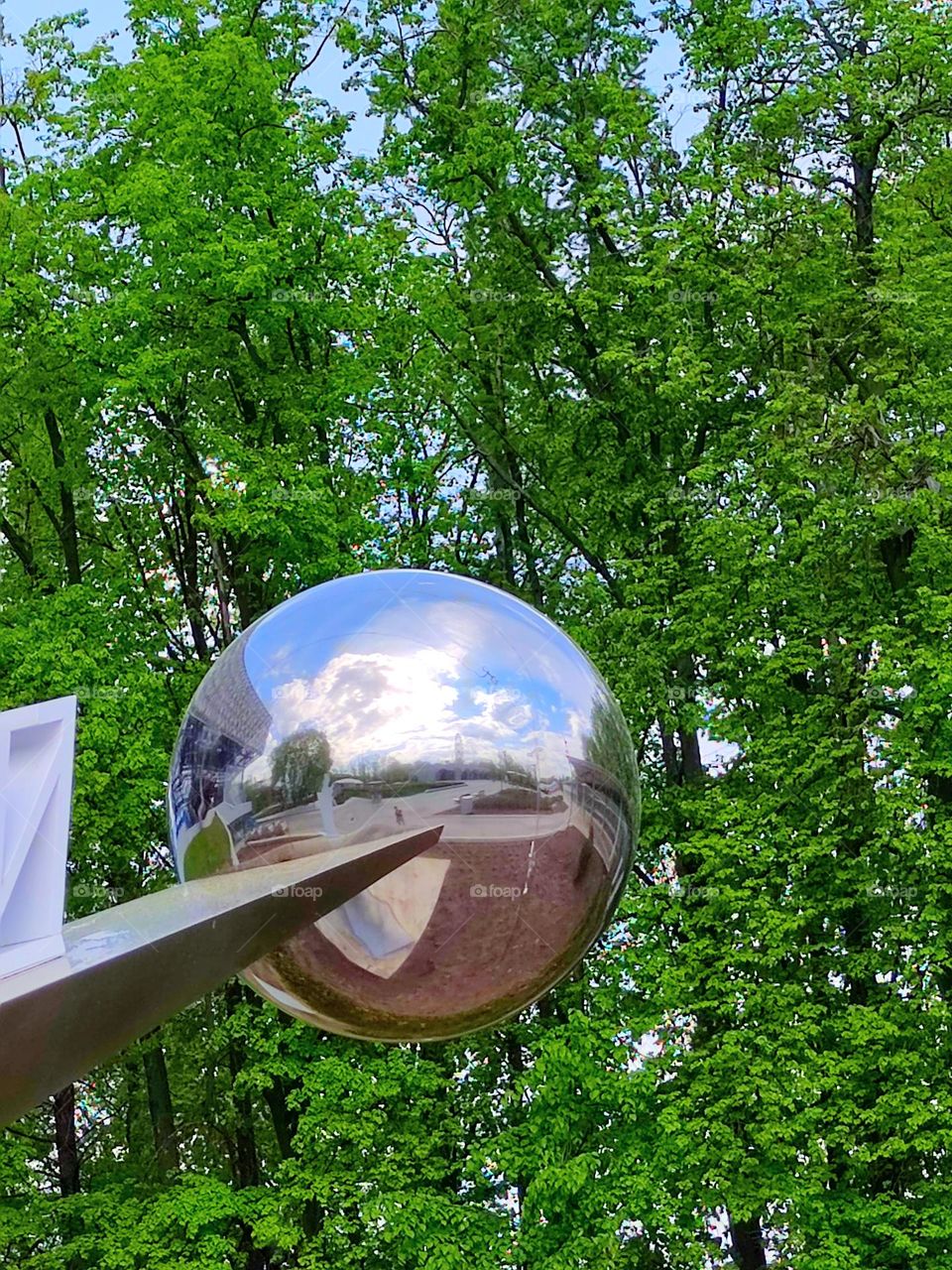 Metal ball on a metal horizontal rod against the background of green trees