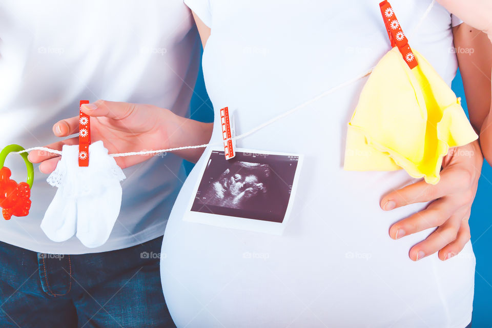 Sonogram picture in front of couple. Ultrasound scan of baby, hat, socks and rattle on clothesline with clothespins in front of expectant parents