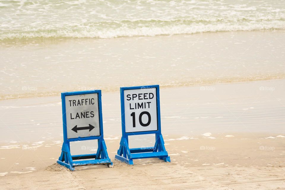 waves rolling up to traffic signs set up on beach sand where cars drive on the beach in Florida USA