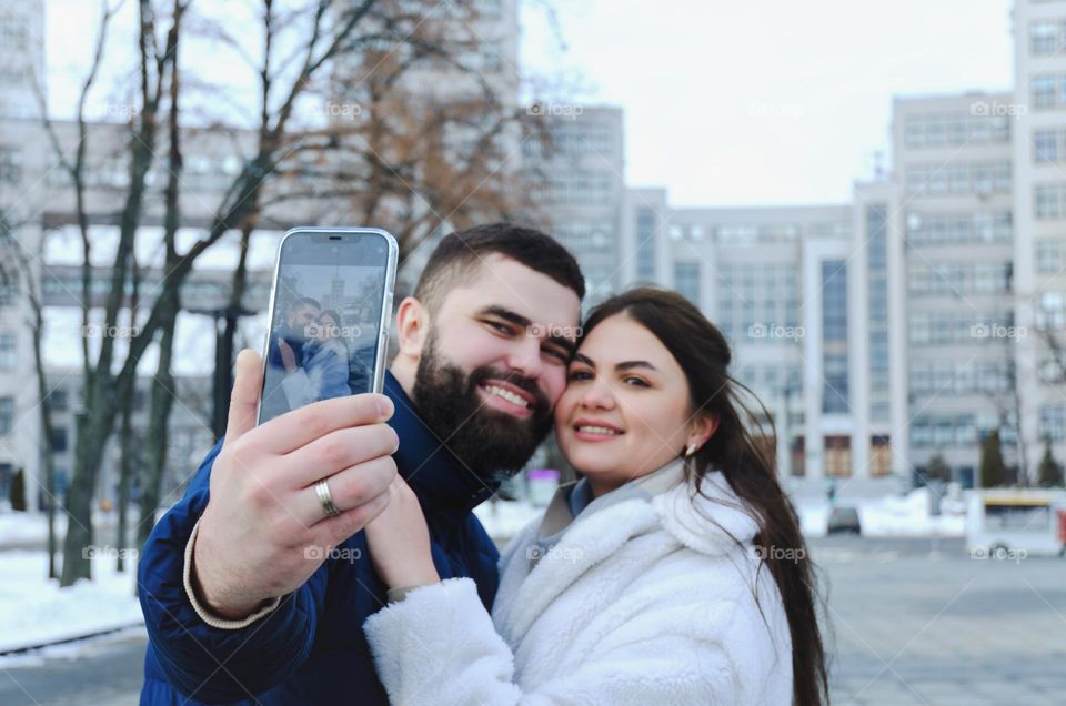 Portrait of young happy couple, bearded man and brunette woman woman relaxing in winter city. Laptop. Phone. Technology. Selfie.  Social media.  Video call