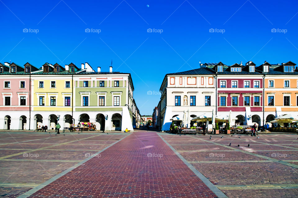 People on Great Market in Zamość, Poland by buildings against clear blue sky.