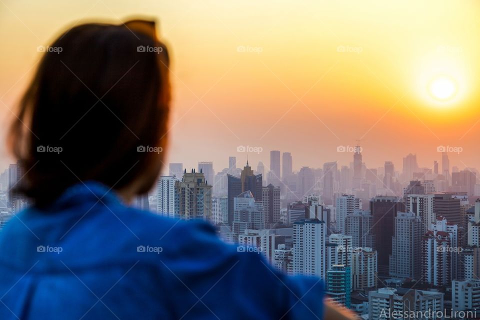 Rear view of a woman looking at city at sunset