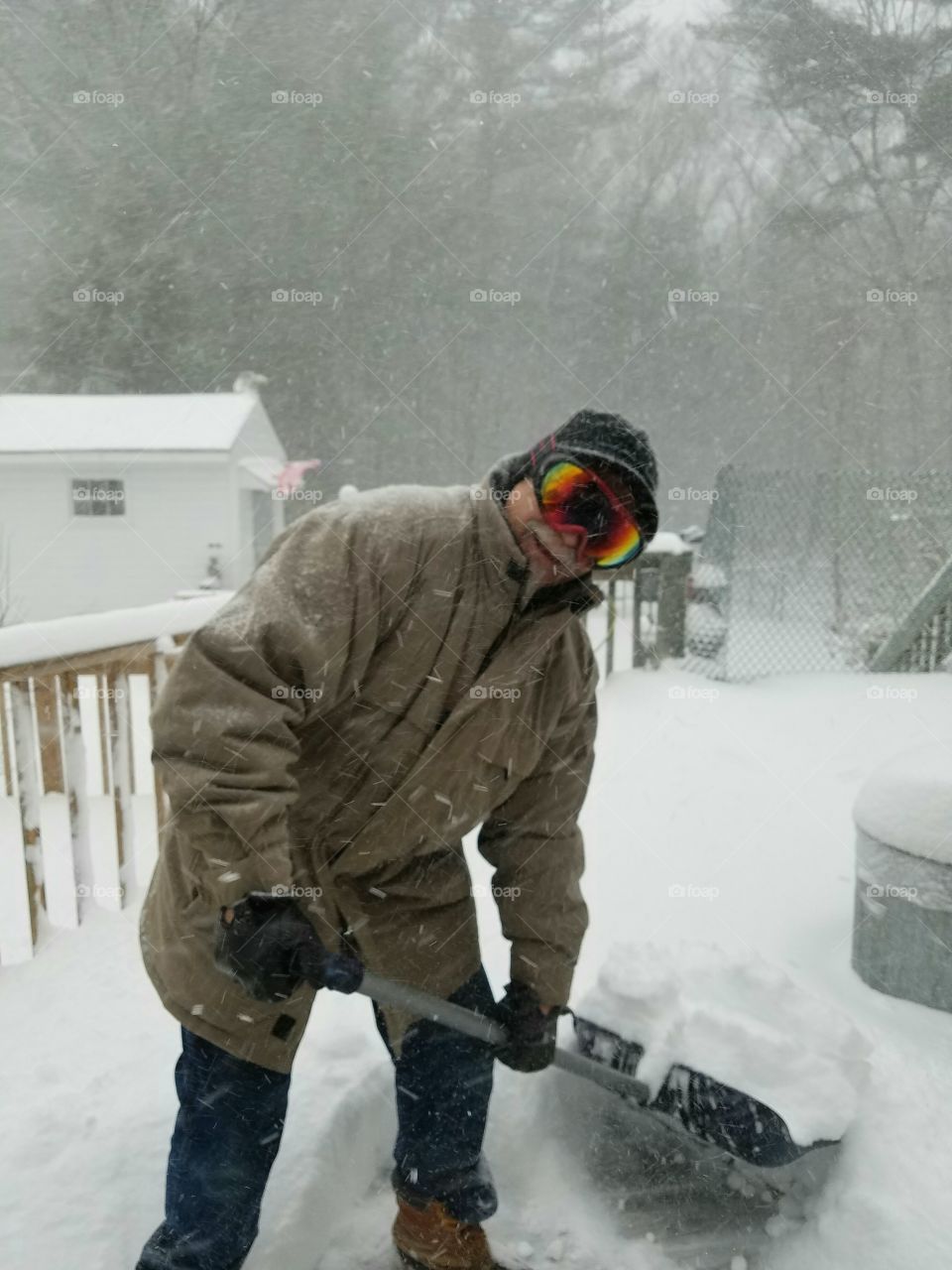Man, goggles, shoveling snow off deck. Blizzard snowstorm