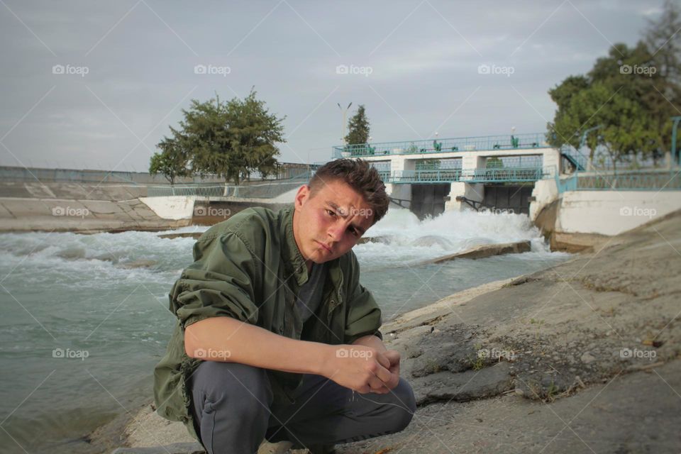 portrait of a young man on the shore of the dam. the fisherman is squatting.