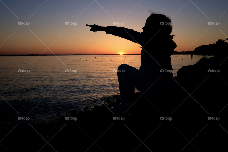 Little girl pointing silhouetted by the golden sunset at the mouth or estuary of the Neuse River in Arapahoe North Carolina. 