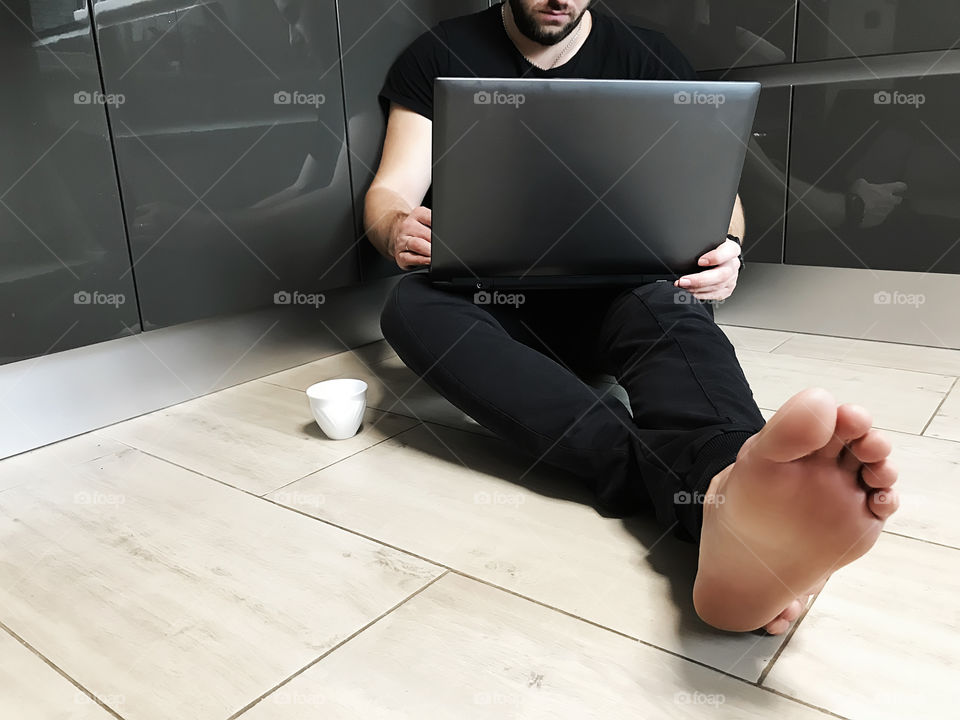 Young barefoot man using a favorite laptop and drinking his morning coffee at home 