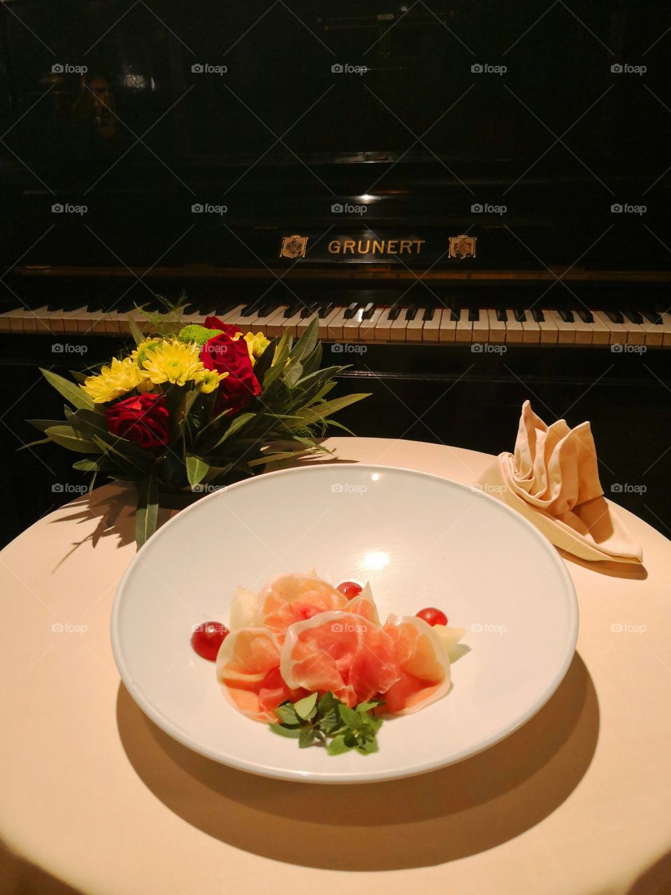 Prsut Melone with flower and piano in the background.