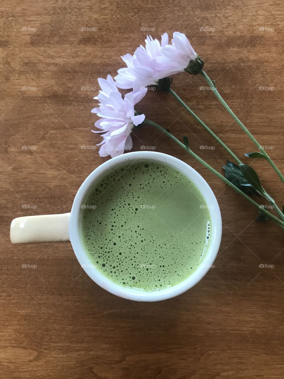 Cup of matcha green tea on wooden table with pastel pink flowers 