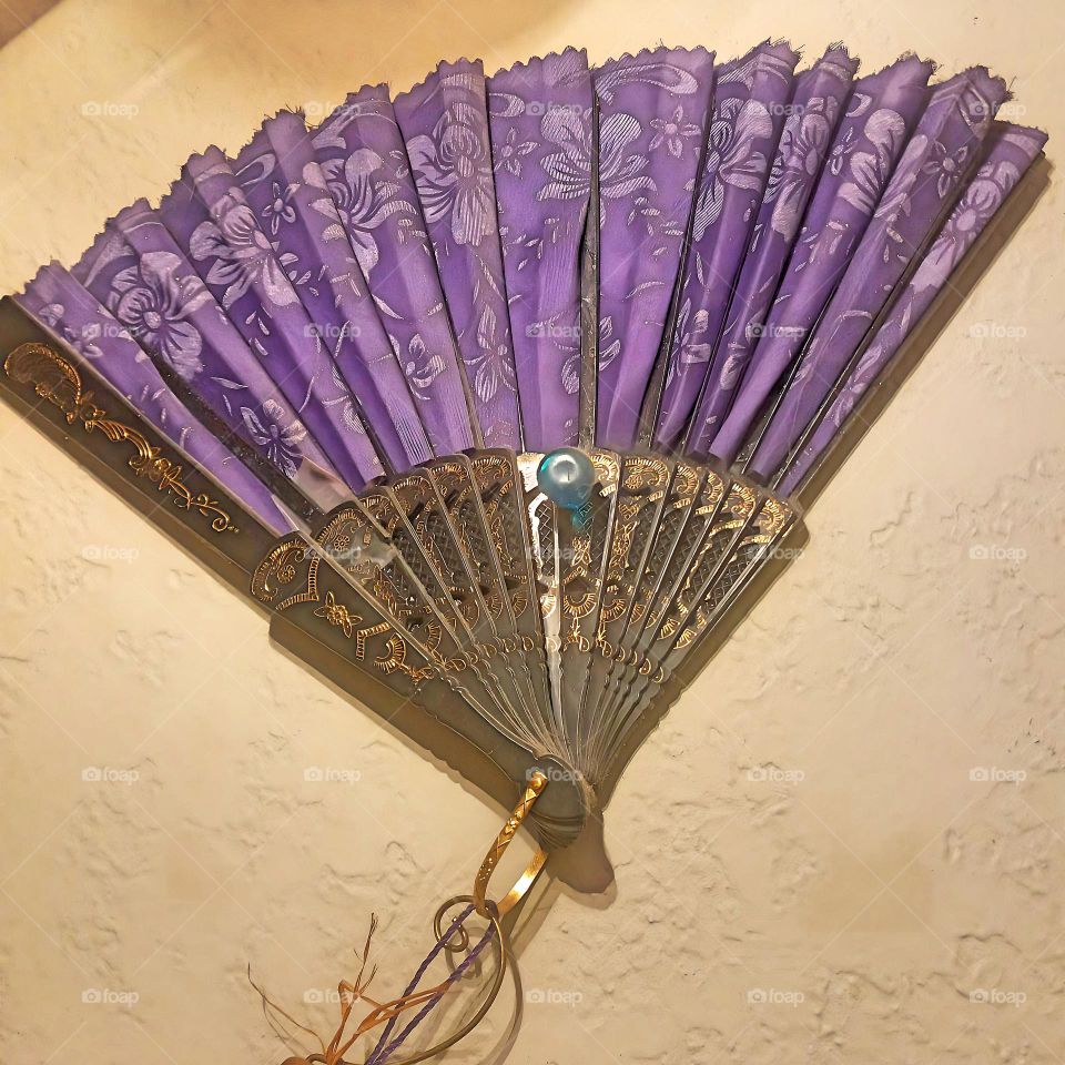 An elegant fan with a light purple background, sprinkled with dainty flowers and finished with delicate gold highlights.