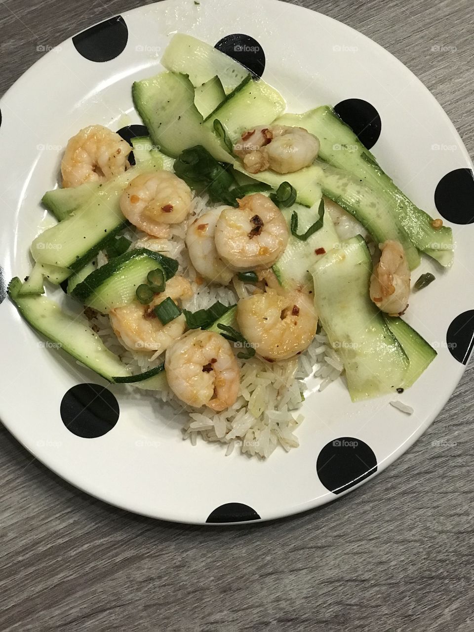 Shrimp and zucchini and rice dish on polka dot black and white plate