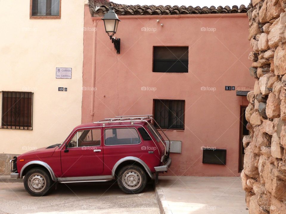 An old red 4x4 type car parked in front of a village house. in small villages poorly served by public transport, the car is essential for commuting.