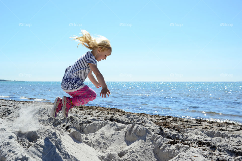 Young girl jumping at the beach and playing in the sand.