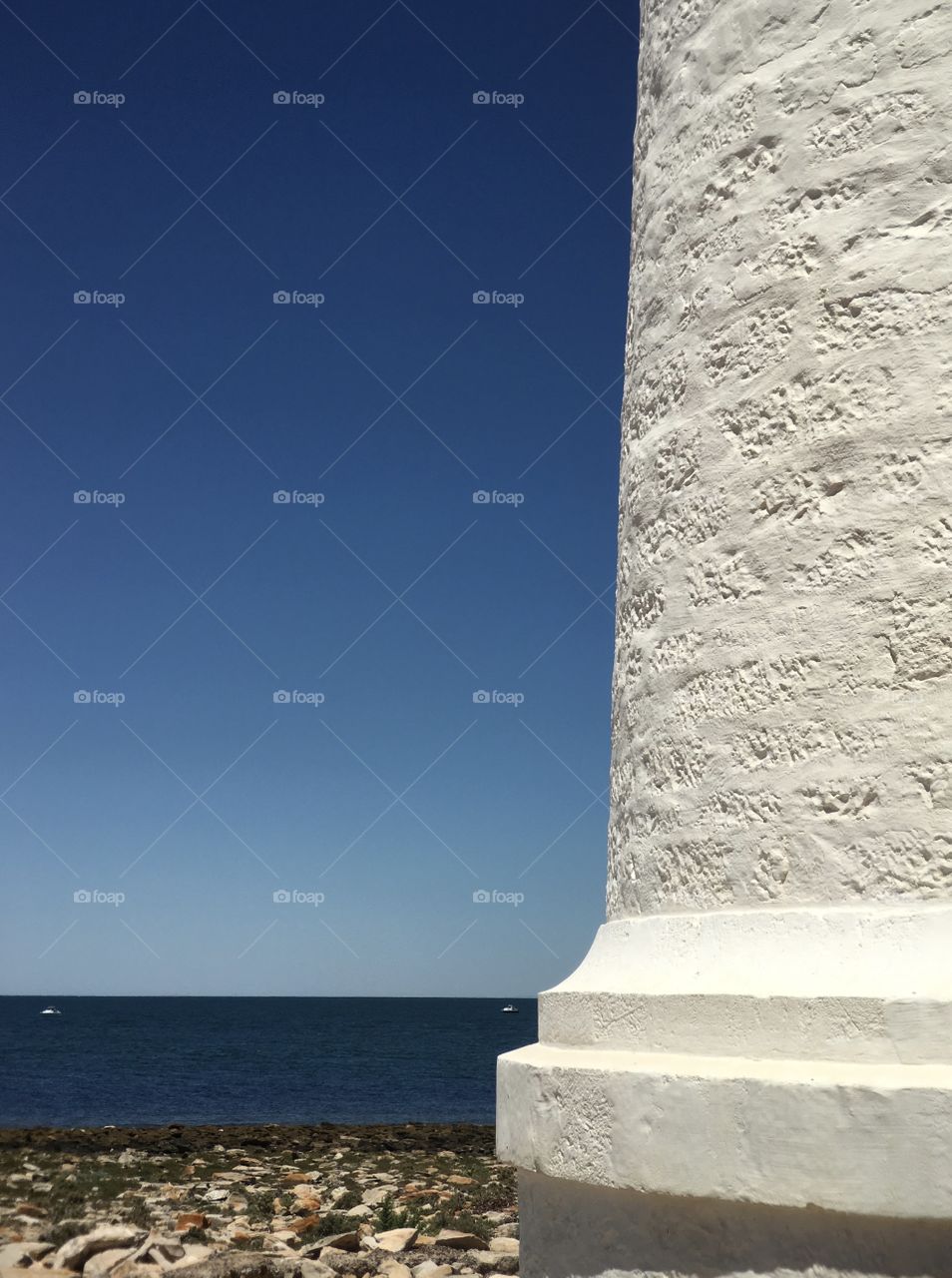 Side of pure white old lighthouse looking out toward the ocean on vivid blue day minimalist image worth space for text