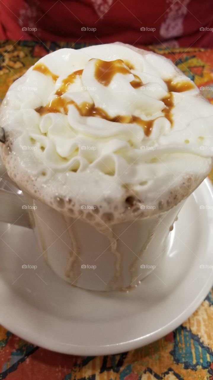 A closeup of a mug filled with hot chocolate, with whip cream and caramel dripping on the sides.