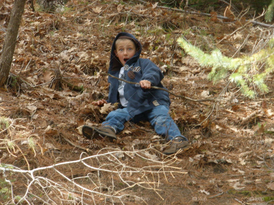 Surprise Slide. Young boy sliding down a hill in the woods with a surprised expression on his face. 