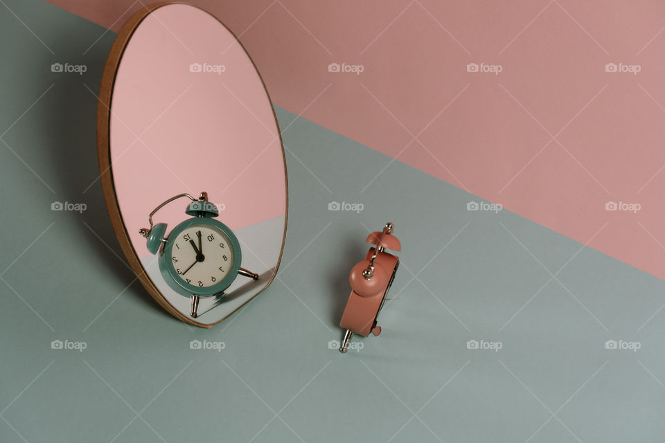 Pink clock in a mirror with a blue reflection. Creative time concept