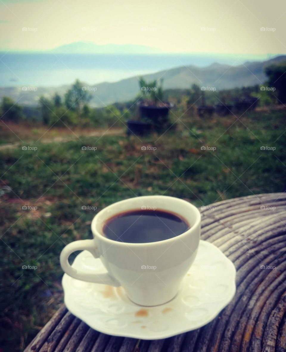 A cup of hot coffee in a small china cup up in the mountains in a cold morning