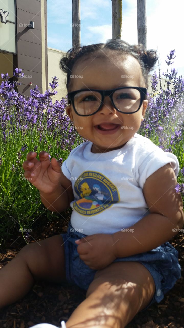 Cute girl sitting on flower field with eyeglasses