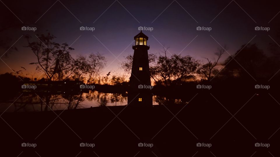 Lighthouse captured during Features of the Night. Reflections of the Colorful Night Sky on Lake Waters sling with landscape of shore line.