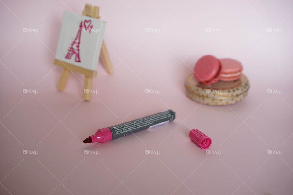 Small easel stand with pink marker and macaroons over pink background