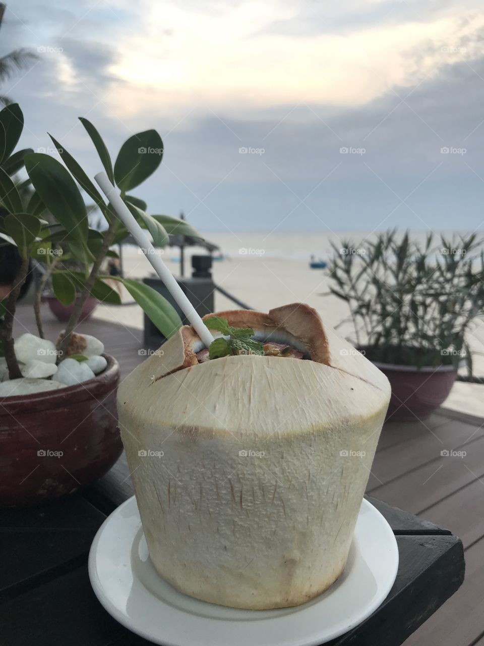 coconut on a black table, with a view of the beach.This’s coconut mojito,new drink at resort I want to try.On the table and in front of me there are many bonsai pots,enjoying drinking while watching the sunset on the sea it's wonderful