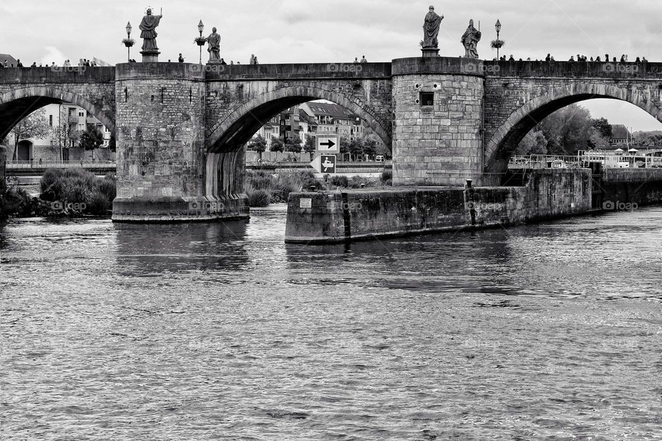 The river Main flows under a bridge with people and statues in Würzburg