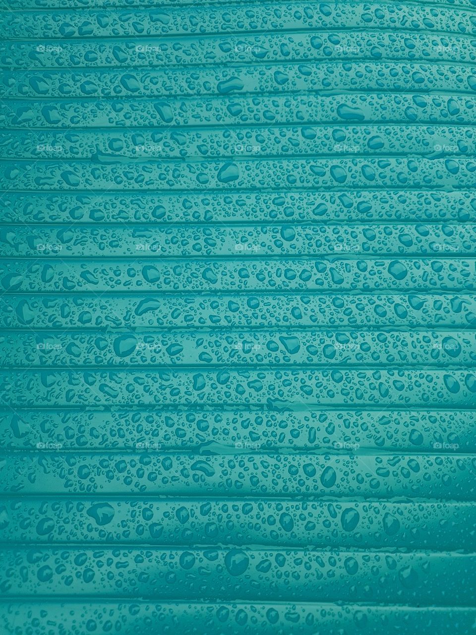 Close up of water droplets on a wet shiny plastic surface turquoise blue green with horizontale lines parallele