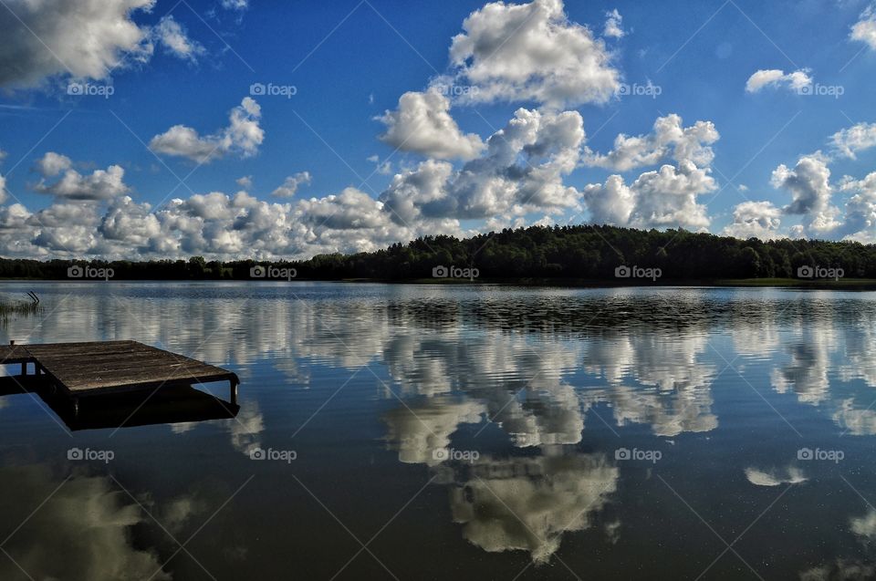 wodden pier and forest on the horizon view on sunny day at the lake in polish countryside, cloudy sky