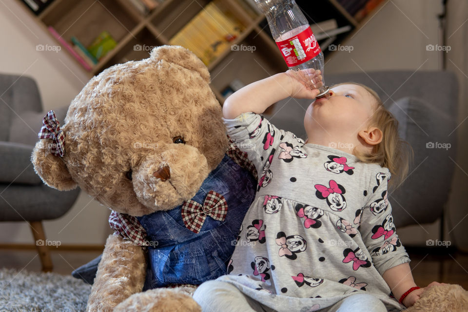 Girl drinking last drops of coca cola with teddy bear