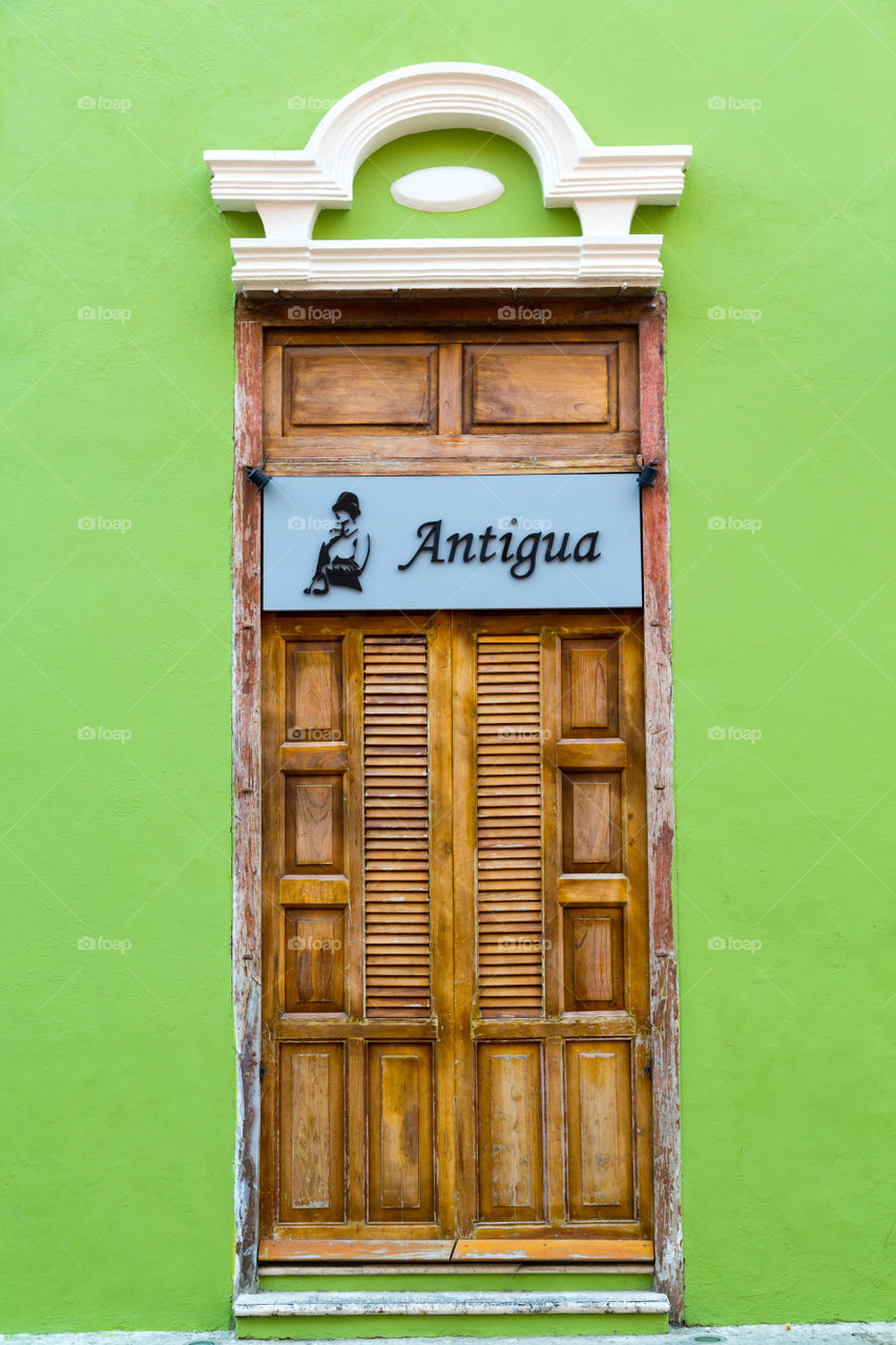 Wooden door of an antique shop. Wooden double door. Sign saying antique. Green wall. Used and worn. Old looking. Newly painted green wall