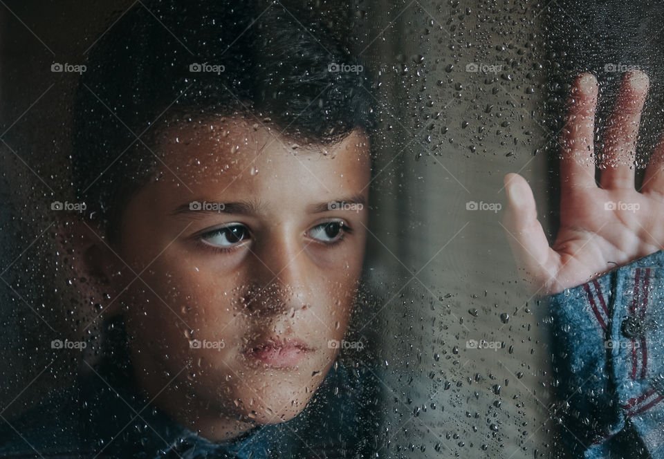 Close-up portrait of boy looking away at the window during rain